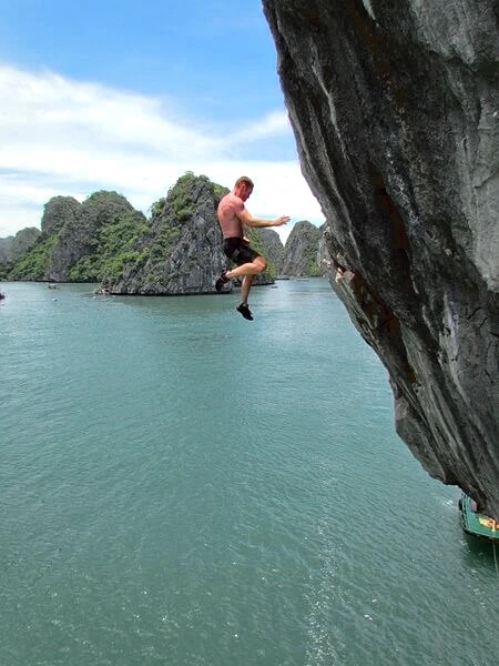 A climber leaving the cliff above the water with limestone islands beyond