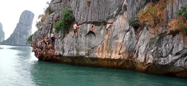 Climbers traversing a limestone sea cliff above green water