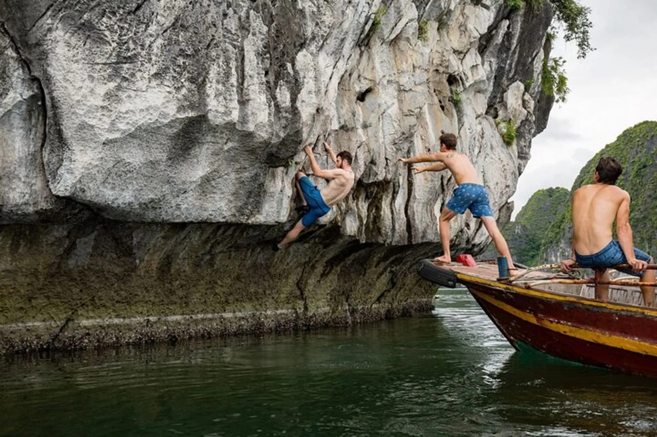 A climber on a limestone wall above the water beside a support boat