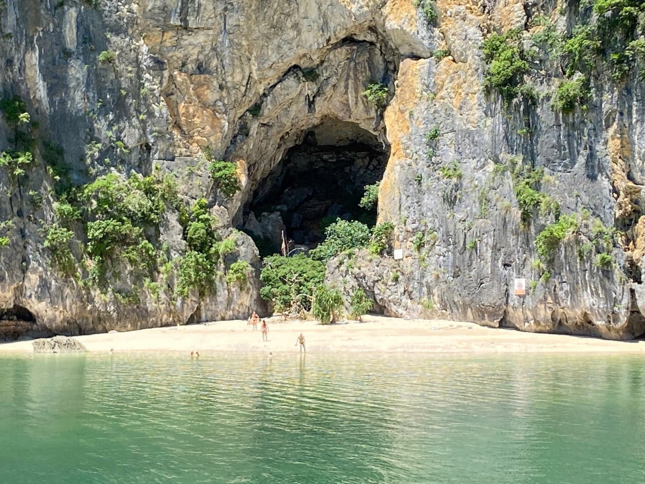 A small sandy beach beneath a limestone cliff and cave entrance