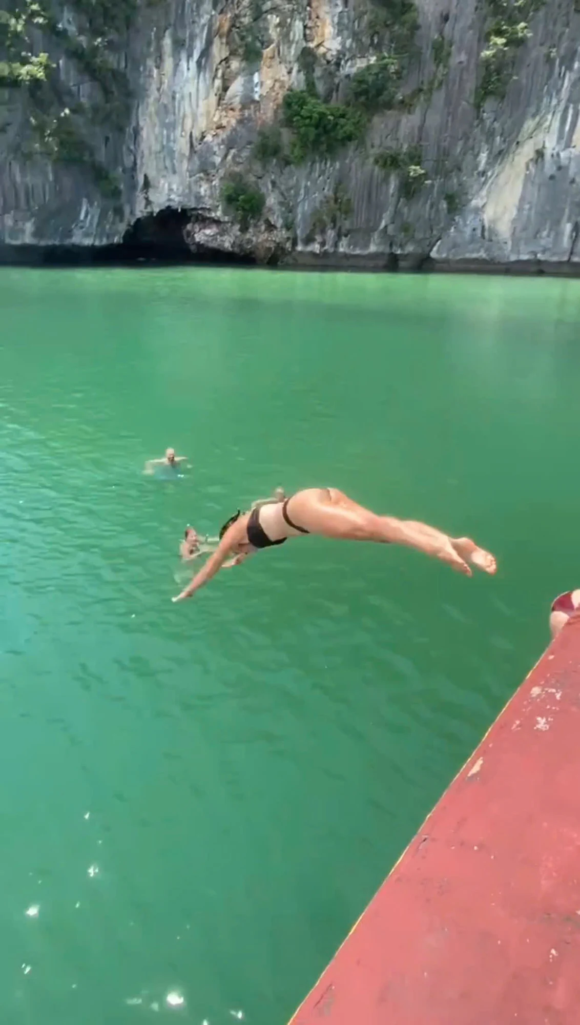 A visitor diving from a boat into the green water of Lan Ha Bay