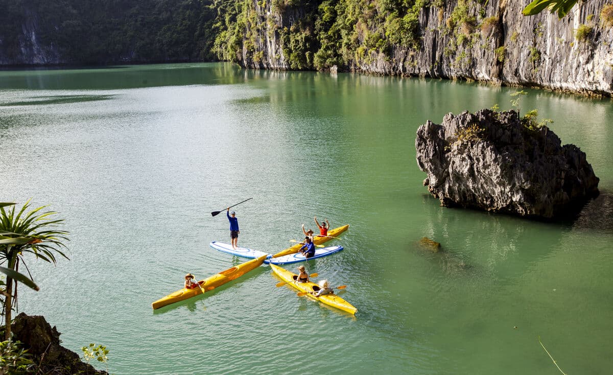 Group of kayakers paddling between limestone cliffs in Lan Ha Bay