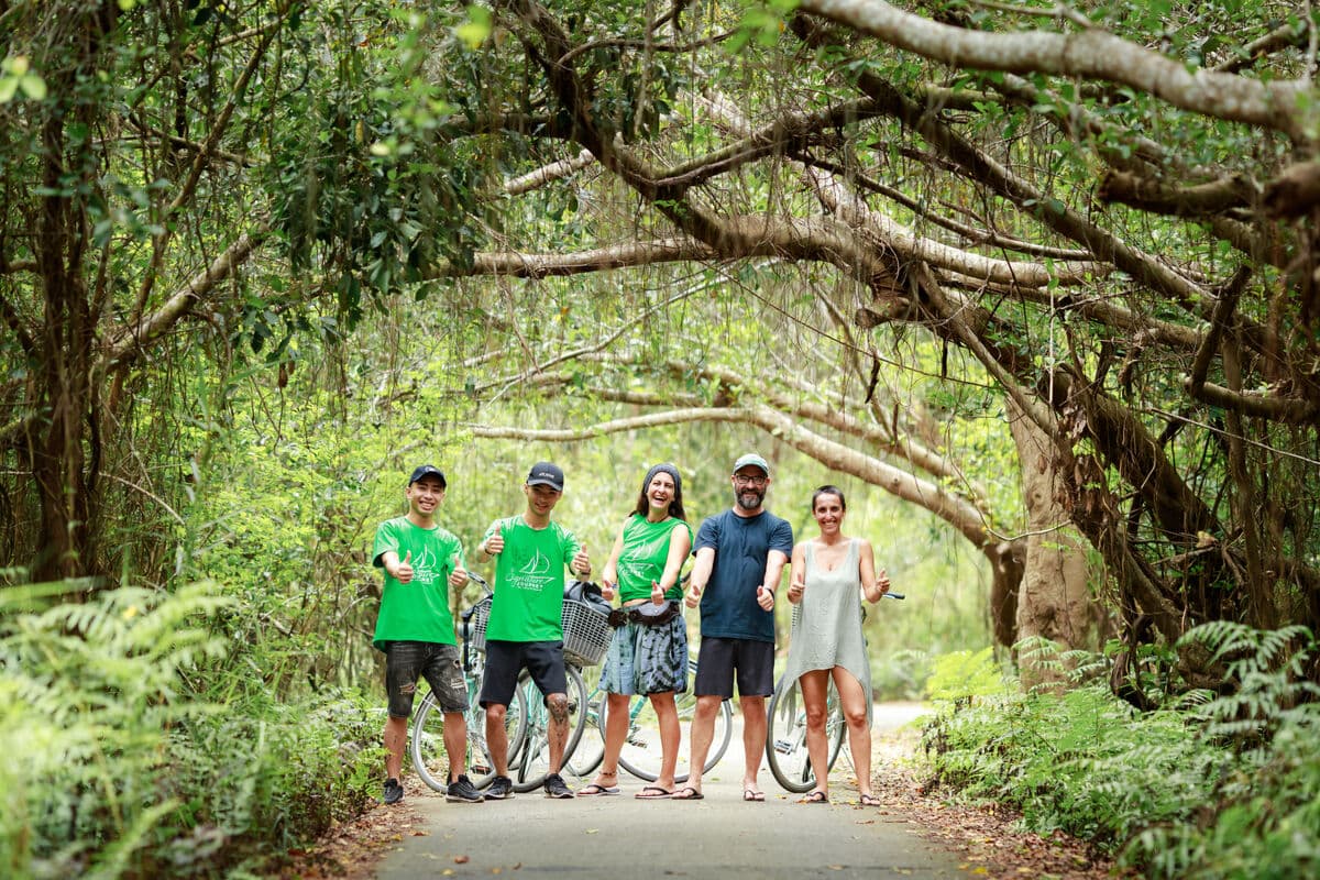 Five travelers with bicycles under a banyan tree canopy in Viet Hai Village